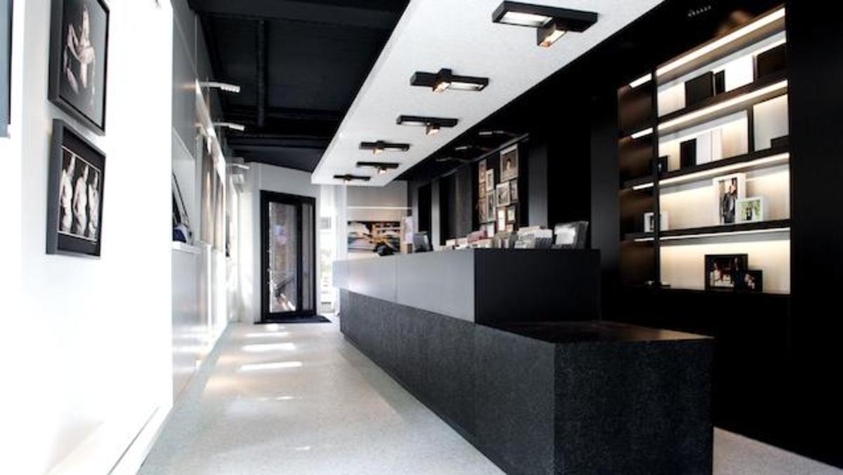 Moderner Empfangsbereich mit minimalistischer Einrichtung Stilvoller Empfangsbereich mit schwarzem Tresen, beleuchteten Regalen, modernen Deckenleuchten und gerahmten Bildern an den Wänden in einem hellen und offenen Raum.